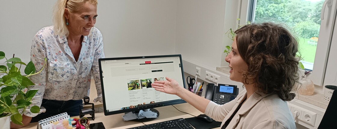 Zwei Frauen im Büro, sie sprechen miteinander, eine von ihnen ist am Laptop.